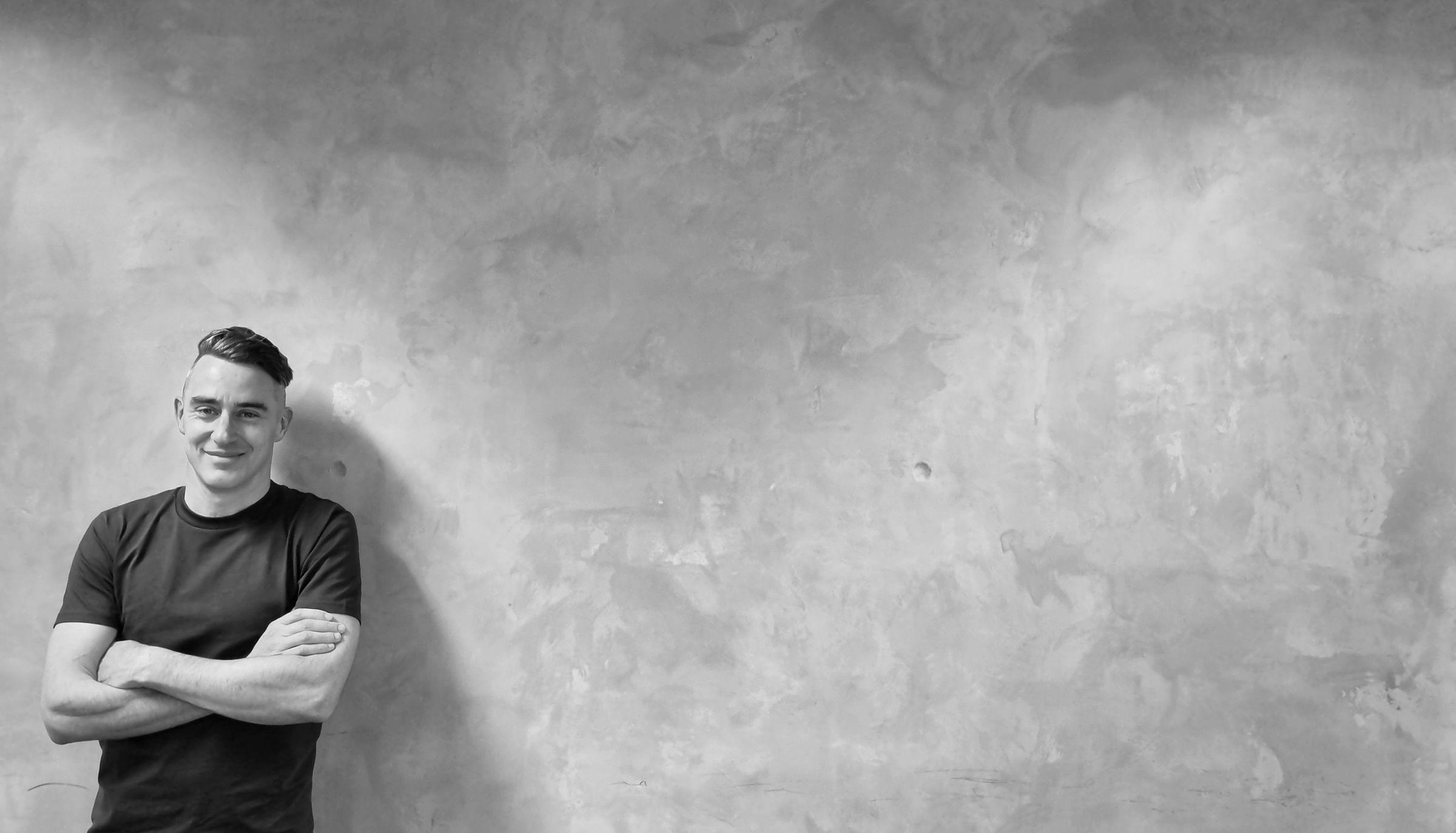 Nathaniel Miller standing next to a stark grey concrete wall - black and white photo